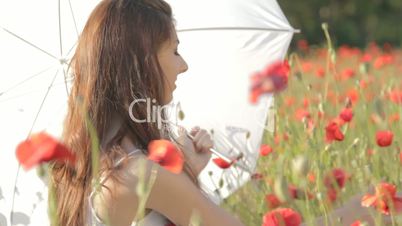 Young woman with white umbrella sitting on chair among poppies