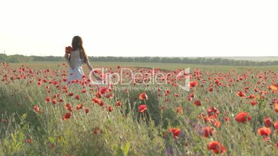 Young woman in white sundress walking through red poppies field