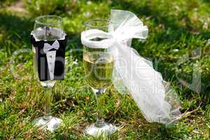 two glasses of champagne in the clothes of bride and groom stand