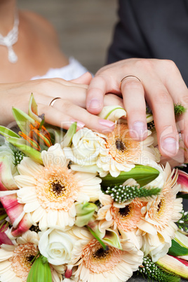 the hands of the bride and groom lying on the bridal bouquet