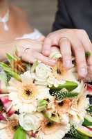 the hands of the bride and groom lying on the bridal bouquet