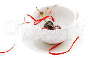 cup saucer  and cherries with ribbon isolated on white