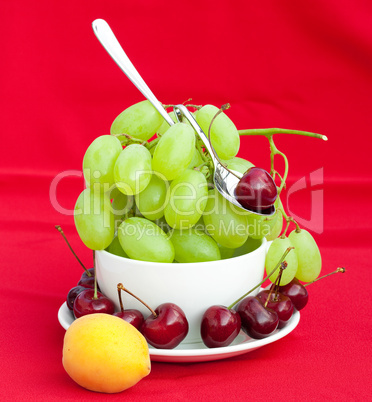 Spoon grapes cherry and apricot in the cup on a red background