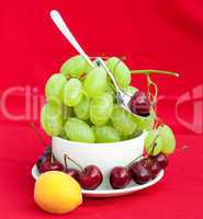 Spoon grapes cherry and apricot in the cup on a red background