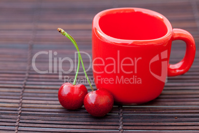 two cherries and a red cup on a bamboo mat