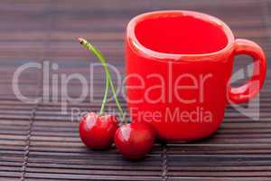 two cherries and a red cup on a bamboo mat