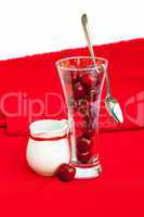 milk jug with a ribbon , glass of cherry and spoon on a red back