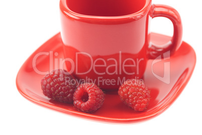 Raspberries in a red cup and saucer isolated on white