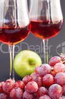 a glass of wine, apple and grape on a black background
