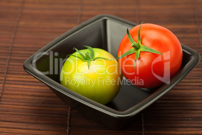 green and red tomatoes in a bowl on a bamboo mat