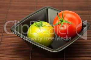 green and red tomatoes in a bowl on a bamboo mat