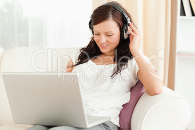 Dark-haired woman relaxing on a sofa with headphones and a noteb