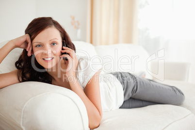 Smiling woman on the phone lying on a sofa