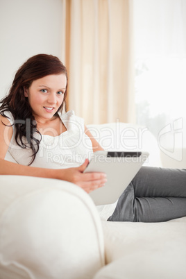 Beautiful woman relaxing on a sofa with a tablet looking into th