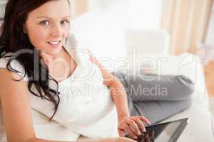 Cute red-haired woman lying on a sofa with a tablet looking into