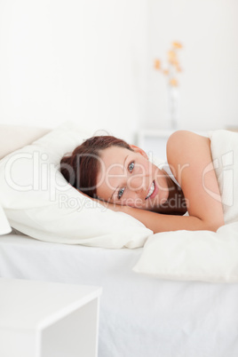 Red-haired woman lying in bed smiling into camera
