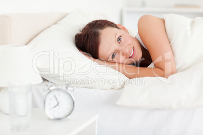 Red-haired woman lying in bed looking into the camera