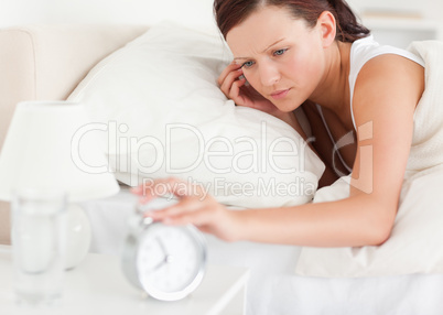 Close up of a Red-haired woman lying in bed turning off alarm cl