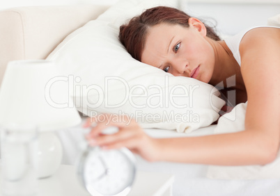 Red-haired woman lying in bed turning off alarm clock