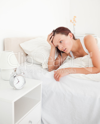 Cute red-haired woman waking up looking at the alarm clock