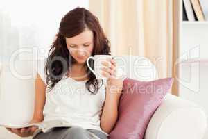 Woman holding a cup while reading a magazine