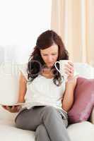 Young Woman holding a cup while reading a magazine