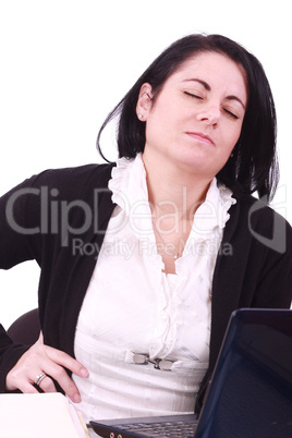 Young woman sitting at her laptop with a lot of work in front of her. She has a pain in her neck / back