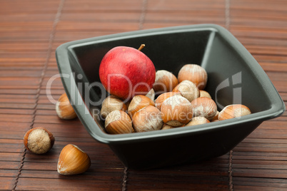 hazelnuts in a bowl and apples on a bamboo mat