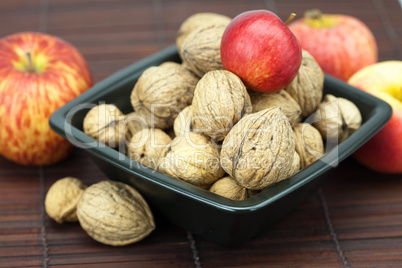 walnuts and apples in a bowl on a bamboo mat