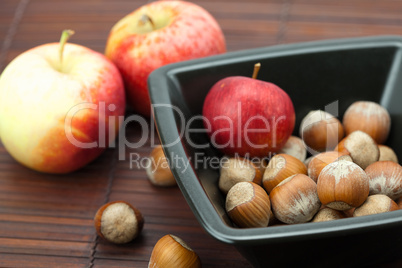 hazelnuts in a bowl and apples on a bamboo mat