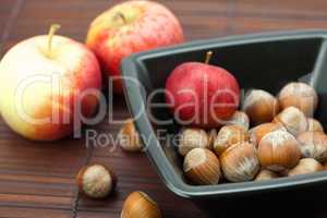 hazelnuts in a bowl and apples on a bamboo mat