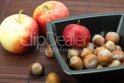 hazelnuts in a bowl and apples on a bamboo mat