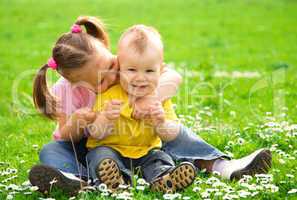Two children are sitting on green meadow