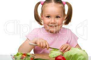 Little girl is cutting carrot for salad