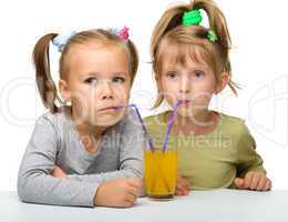 Two little girls are drinking orange juice