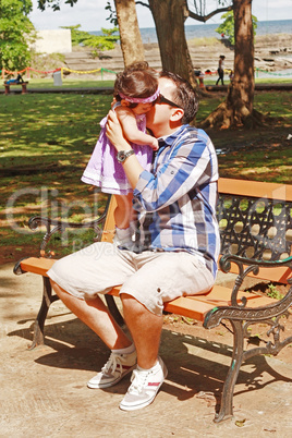 A father holds and kisses his baby with a muted tropical setting