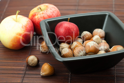 hazelnuts in a bowl and apples on a bamboo mat