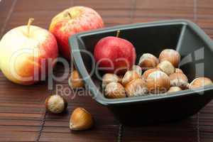 hazelnuts in a bowl and apples on a bamboo mat