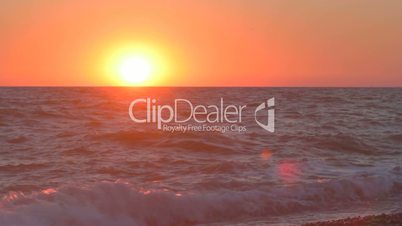 Sunset over the horizon with waves splashing on the beach