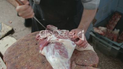 Butcher carving lamb's leg on wooden frame