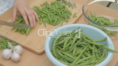 Slicing fresh green string beans on wooden chopping board