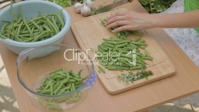 Carving fresh green beans outdoors on wooden chopping board