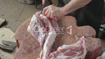 Butcher separating large bone of mutton's leg from meat