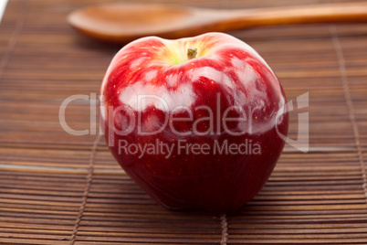 red apple and a wooden spoon on a bamboo mat