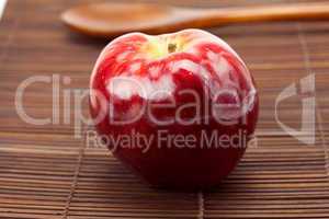 red apple and a wooden spoon on a bamboo mat