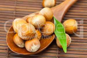 hazelnuts and green leaf on a wooden spoon on a bamboo mat
