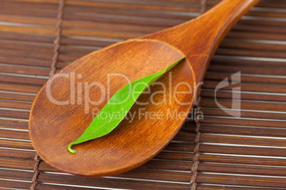 green leaf on the wooden spoon on a bamboo mat
