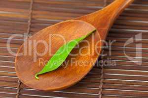 green leaf on the wooden spoon on a bamboo mat