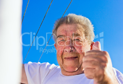 Senior hebt den Daumen hoch bei strahlend blauen Himmel