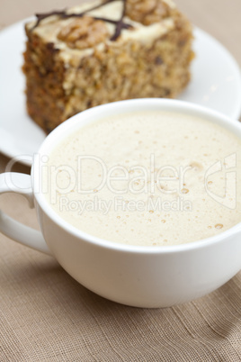 cup of cappuccino, a piece of cake with nuts lying on the plate